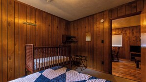 Een kamer met houten lambrisering, een bed, een ledikant, een tafeltje en een televisie.