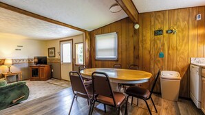 Una habitación acogedora de estilo cabaña con interior de madera, una mesa de comedor con sillas, un televisor y una zona de cocina con lavavajillas.