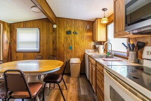 A compact kitchen with wooden walls, a round dining table, and basic amenities. - Peaceful Cabin on Kentucky Lake (Benton)