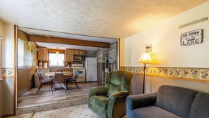 Una sala de estar acogedora con un sillón verde y un sofá azul, un comedor con muebles de madera, y una cocina con armarios de madera y un refrigerador blanco.