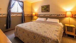 A hotel room with a large bed, two bedside lamps, a window with curtains, a floral-patterned headboard, and a painting on the wall. - Spacious Cabin on Kentucky Lake (Benton)