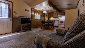 A living room with a sofa, a television, and a dining area with a table and chairs. - Spacious Cabin on Kentucky Lake (Benton)