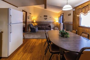A compact kitchen with a refrigerator, dining table, and chairs. A sofa and armchair are in the adjacent living area. - Spacious Cabin on Kentucky Lake (Benton)
