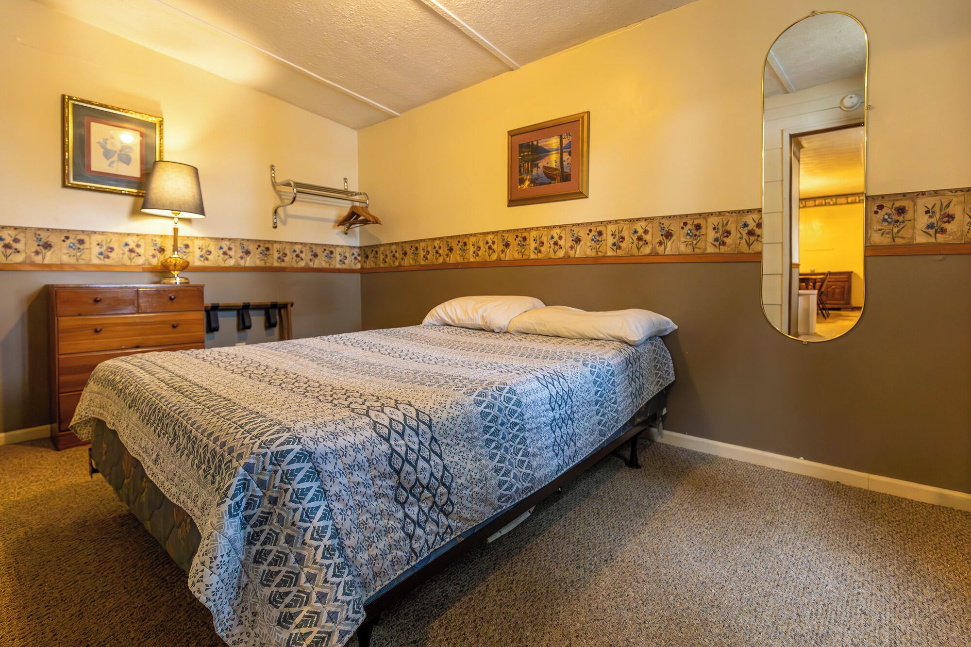 Une chambre à coucher comprenant un lit, une commode, un miroir et un motif floral décorant le mur.