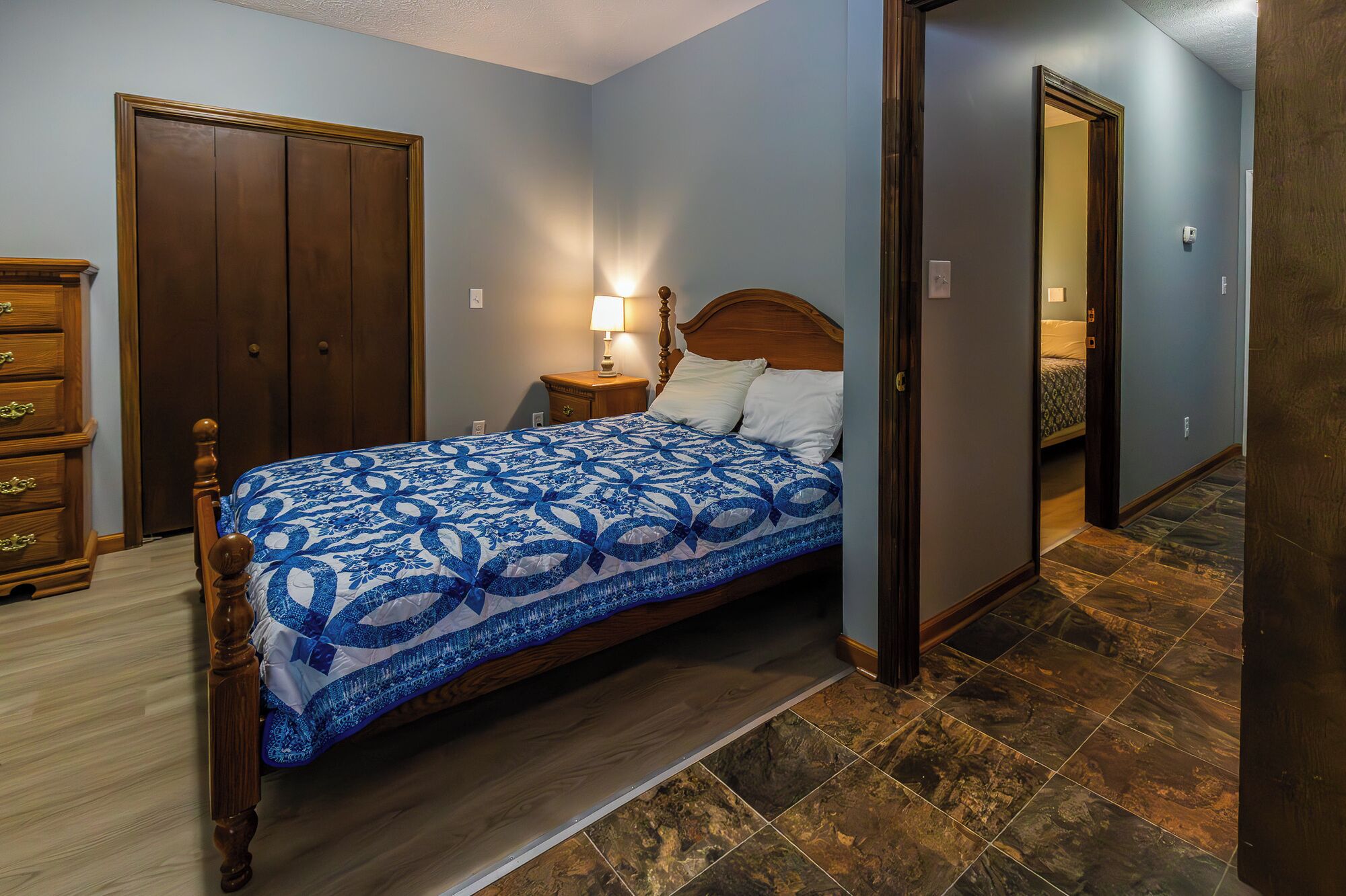 Een slaapkamer met een bed, een houten dressoir en een nachtkastje met een lamp.