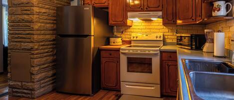 Una cocina con detalles en pared de piedra, armarios de madera, refrigerador de acero inoxidable, estufa y microondas.