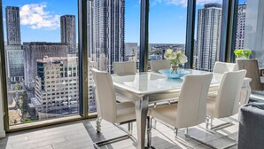 Un espace de restauration moderne avec une table en verre et des chaises blanches, de grandes fenêtres offrant une vue sur la ville.