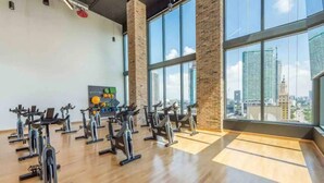 Une salle de sport équipée de vélos d’appartement, d’un support mural pour ballons d’exercice et offrant une vue sur la ville grâce à de grandes fenêtres.