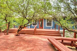 A wooden deck with steps leading to a blue building with a red door, surrounded by trees. - Hill Country Retreat •Hot Tub, Luxury, Sleeps 14! (Austin)