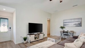 Ein modernes Wohnzimmer mit Flachbildfernseher, einer Couch, einem Couchtisch und einem Schreibtisch mit Stuhl.