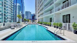 A swimming pool with a 5ft depth marker, surrounded by modern buildings and potted plants. - Luxurious private unit with parking (Miami)