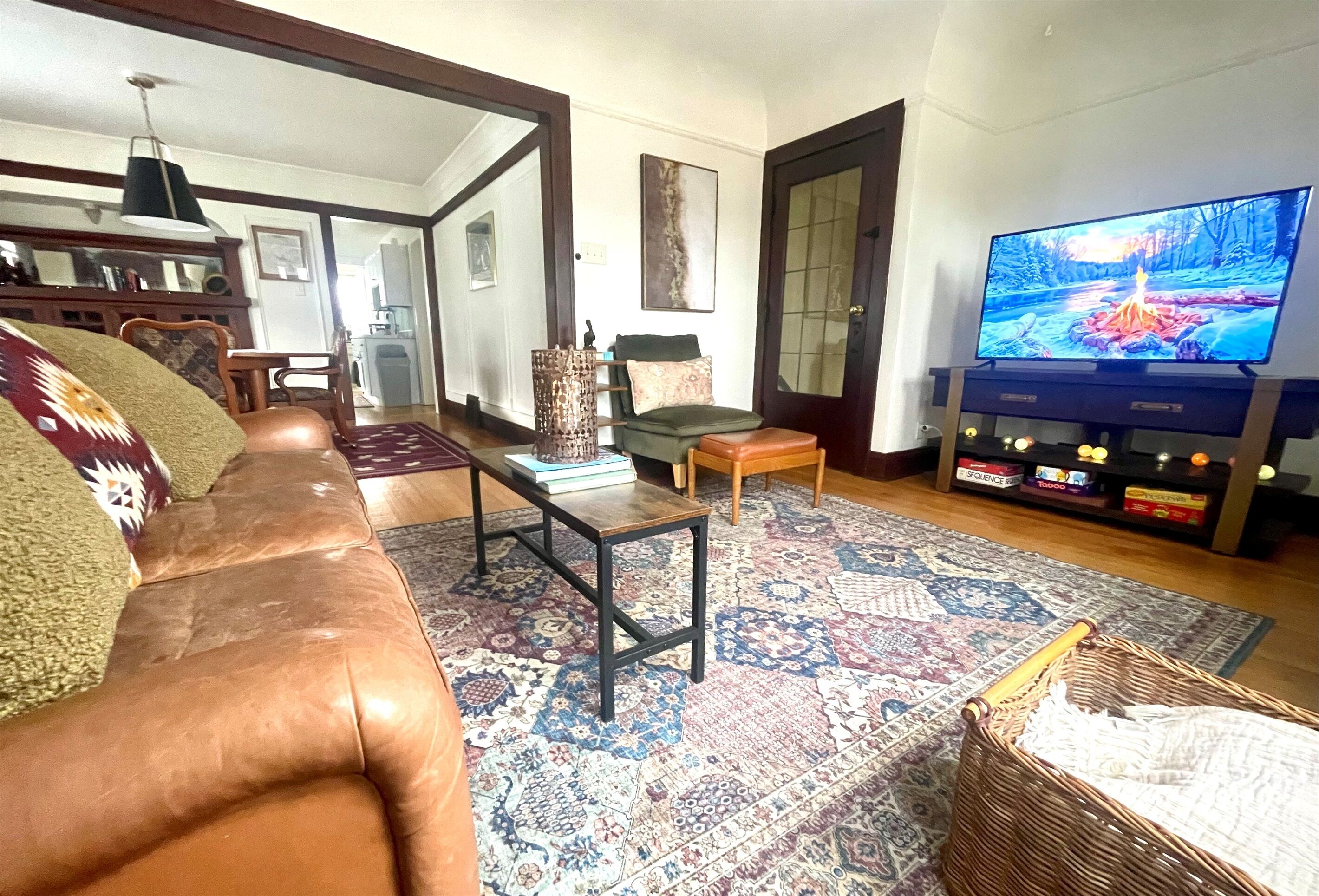 Un salon avec un canapé en cuir marron, un tapis à motifs, un téléviseur et une bibliothèque.