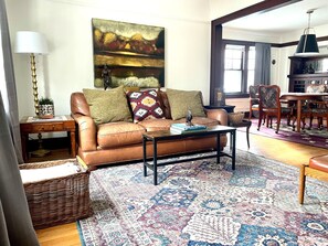Un salon avec un canapé en cuir marron, un tapis à motifs, une table basse et un coin repas comprenant des chaises et une table en bois.