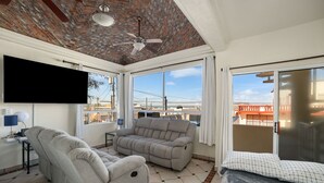 Une véranda avec un plafond en briques, un ventilateur de plafond, une grande fenêtre, un canapé, un fauteuil inclinable et un lit.