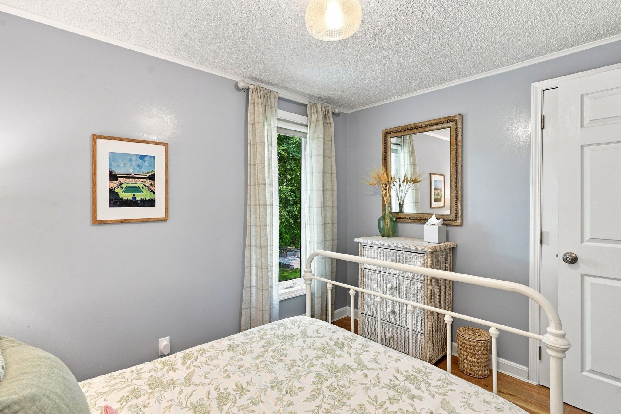A bedroom with a bed, a dresser, a mirror, and a window with curtains.