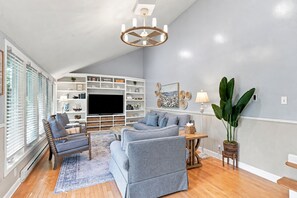 A living room with a TV, sofas, a coffee table, and a bookshelf. - Elegant retreat, 10 min. from Newport; game room, fire pit, & huge deck! (Jamestown)