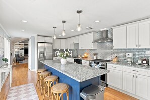 A modern kitchen with a large island, white cabinets, and a blue accent wall. - Elegant retreat, 10 min. from Newport; game room, fire pit, & huge deck! (Jamestown)