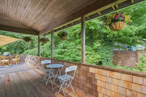 Uma área externa coberta com deck de madeira, cadeiras de metal e uma mesa.