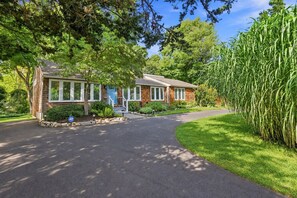 A two-story house with a front entrance, a driveway, and a well-maintained lawn. - Elegant retreat, 10 min. from Newport; game room, fire pit, & huge deck! (Jamestown)