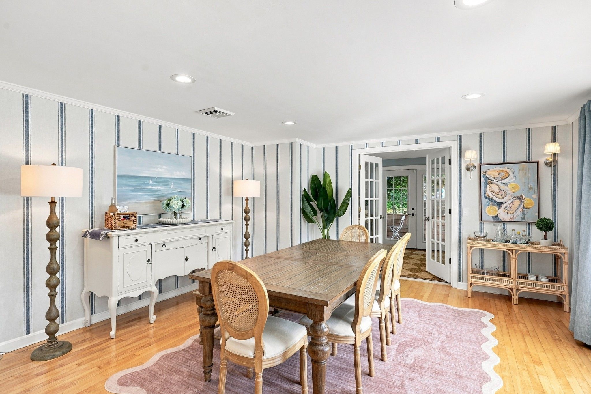 A dining area with a wooden table and chairs, a white cabinet, and striped wallpaper.