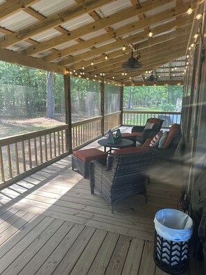 A covered outdoor seating area with wicker furniture, a ceiling fan, and string lights.