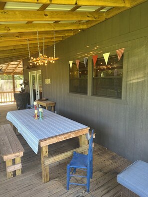 A covered patio area with a wooden table, benches, and a blue chair. - Cozy 2 bedroom cabin on lovely Bear Creek HaleyvilleAl (Haleyville)