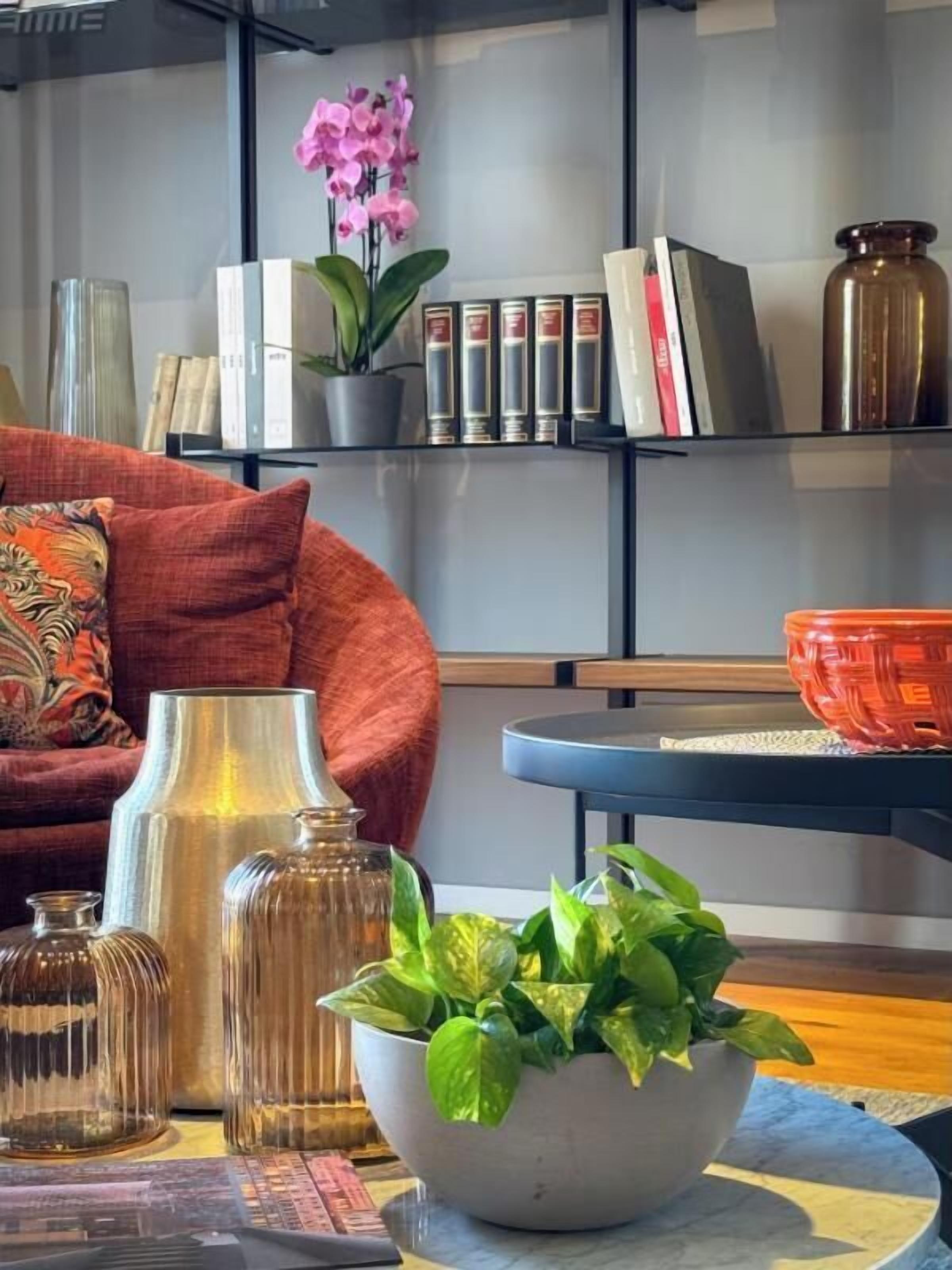 Een moderne woonkamer met een bank, een salontafel, decoratieve vazen, een potplant en een boekenkast met boeken en een roze orchidee.