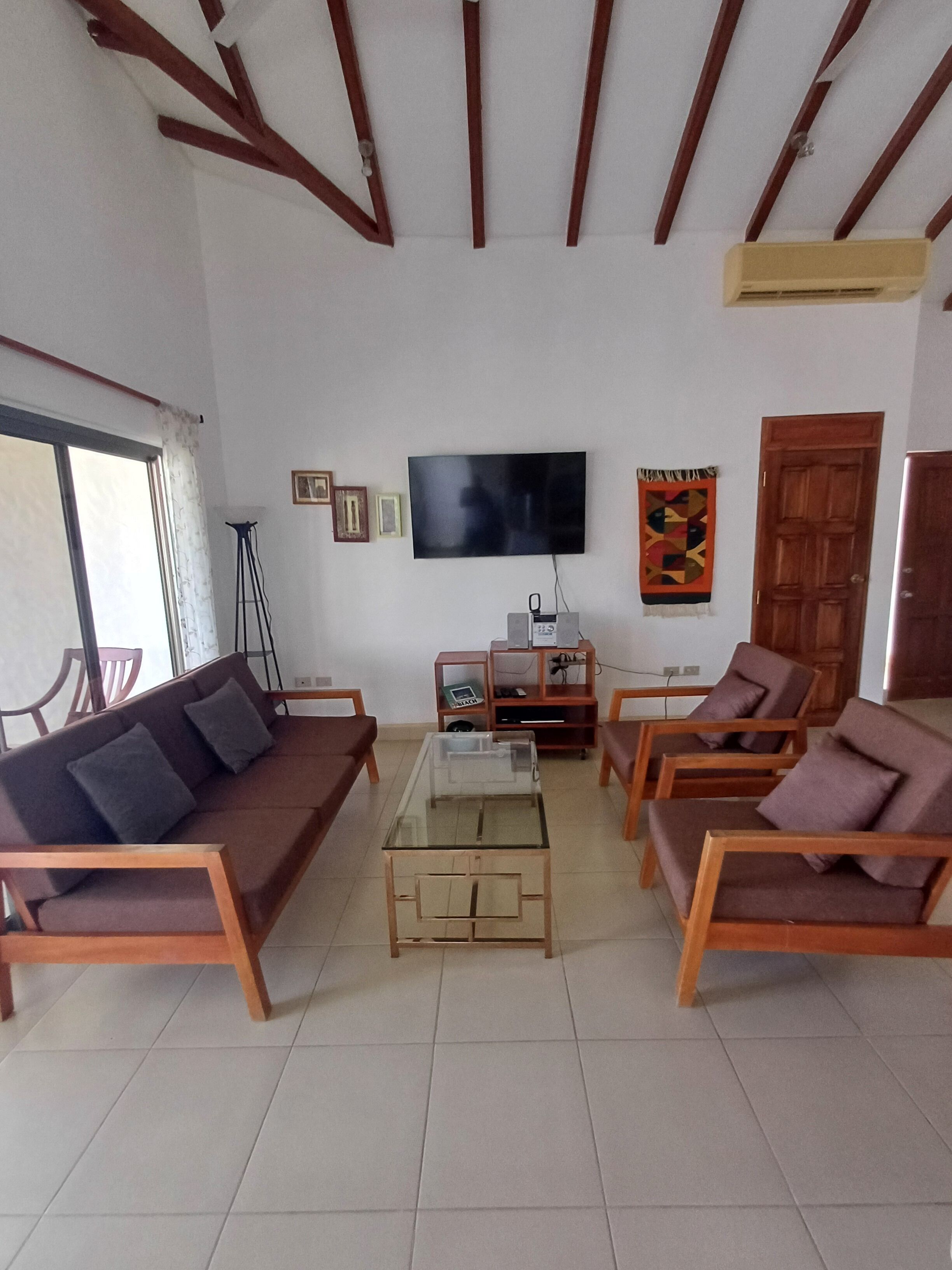 Un salón con sofá, sillones, una mesa de centro, televisión y techo de madera.