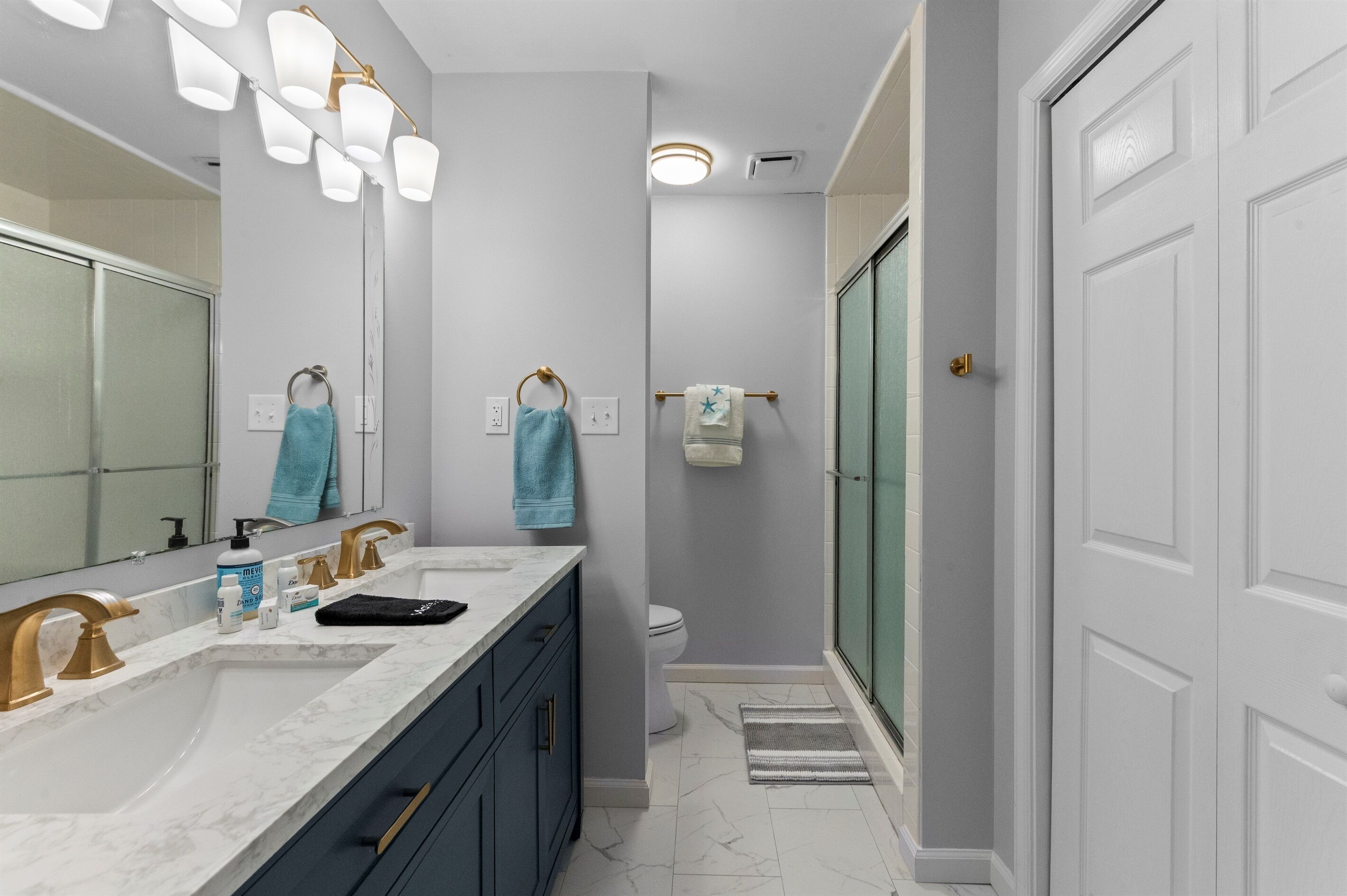A modern bathroom with a large mirror, dual sinks, and a shower area.
