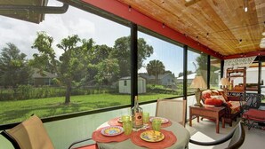 A room with a large window, a table set for dining, and a chair. - Coastal Comfort Retreat - Pet-Friendly Paradise w/ Fenced Yard, Fire Pit & Lanai (Fort Pierce)
