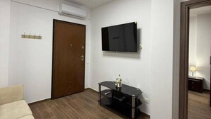 A modern living room with a flat-screen TV mounted on the wall, a wooden door, and a sofa. - Le Grace Urban Retreat Near Near Citycenter Sea (Kalamaria)