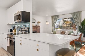 Una cocina moderna con una isla grande, horno empotrado y microondas. Hay un comedor con vistas al exterior.