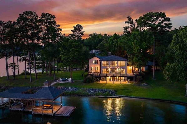 A modern house with a large deck, a dock, and a pond.