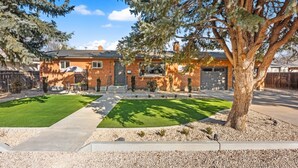 A two-story brick house with a garage, a well-maintained lawn, and a large tree in the front yard. - Welcoming Home near Downtown Boise (Boise)
