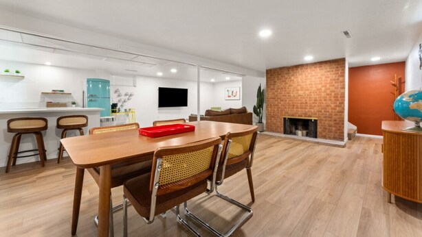 A modern living room with a wooden dining table, wicker chairs, a brick fireplace, and a flat-screen TV mounted on the wall. - Welcoming Home near Downtown Boise (Boise)