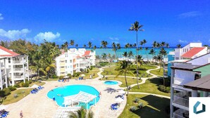 Resort com várias piscinas, palmeiras e vista para a praia.