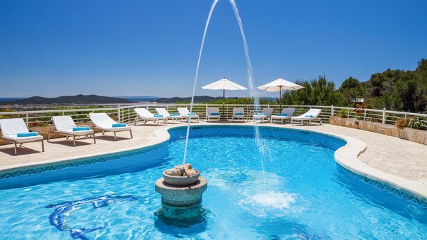 A swimming pool with lounge chairs and umbrellas, surrounded by a stone deck and a view of the landscape. - Teresa Fontalba_Ses Casetes (Sant Jordi de Ses Sali)
