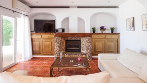 A spacious living area with a stone fireplace, wooden cabinets, and a large TV. - Teresa Fontalba_Ses Casetes (Sant Jordi de Ses Sali)