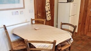 A dining area with a round table, four wooden chairs, a white tablecloth, a microwave, and a refrigerator.