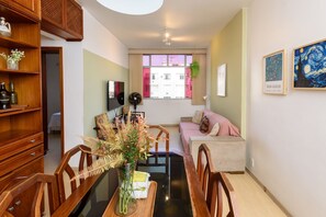 Ein Wohnzimmer mit Esstisch, Stühlen, einer Couch, einem Ventilator und Kunstwerken an den Wänden.