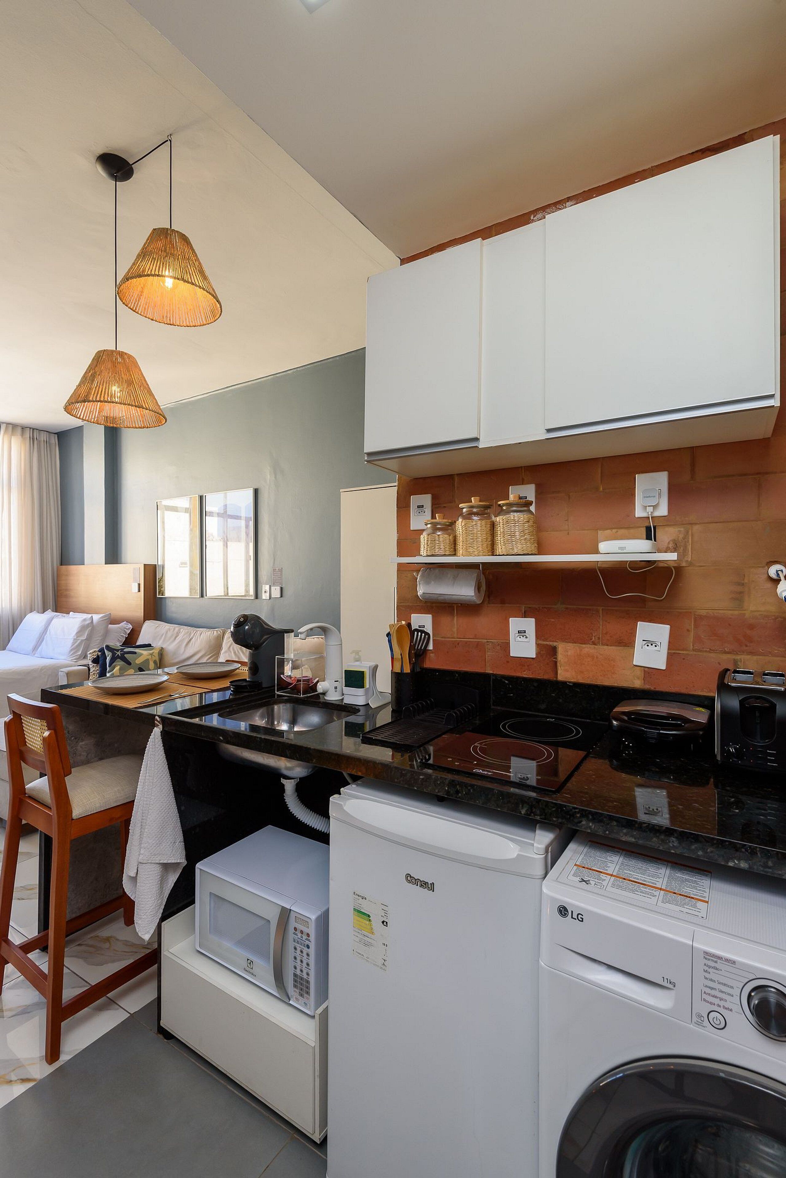 Cozinha moderna com armários brancos, micro-ondas, máquina de lavar LG e luminárias pendentes de vime.
