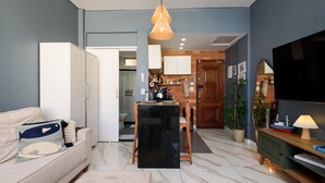 Uma sala de estar com sofá, mesa de jantar, televisão e cozinha ao fundo.