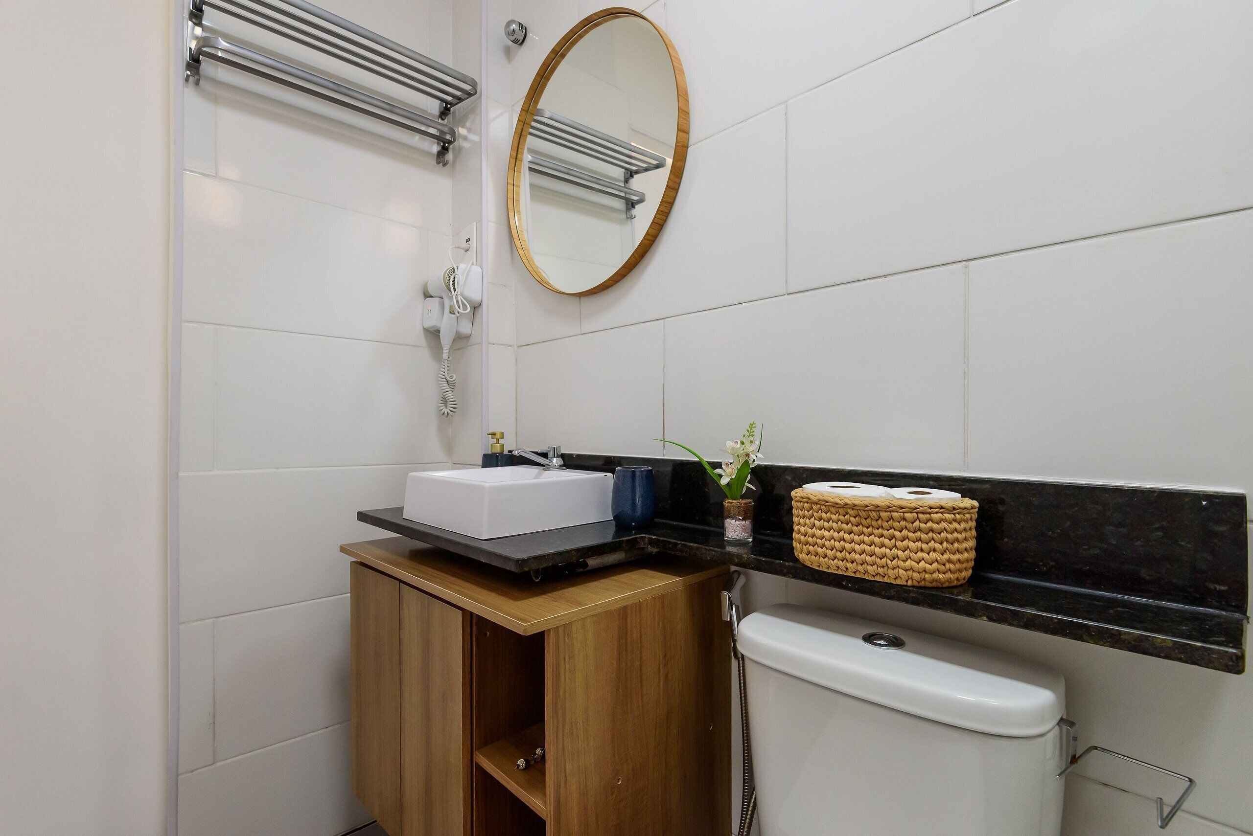 A bathroom with a white sink, wooden cabinet, black countertop, and a toilet.