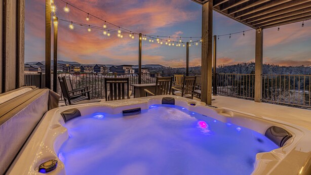A hot tub with a view of a snowy landscape, surrounded by wooden furniture and string lights.