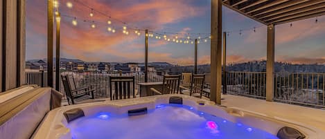 Un jacuzzi con vistas a un paisaje nevado, rodeado de muebles de madera y luces colgantes.