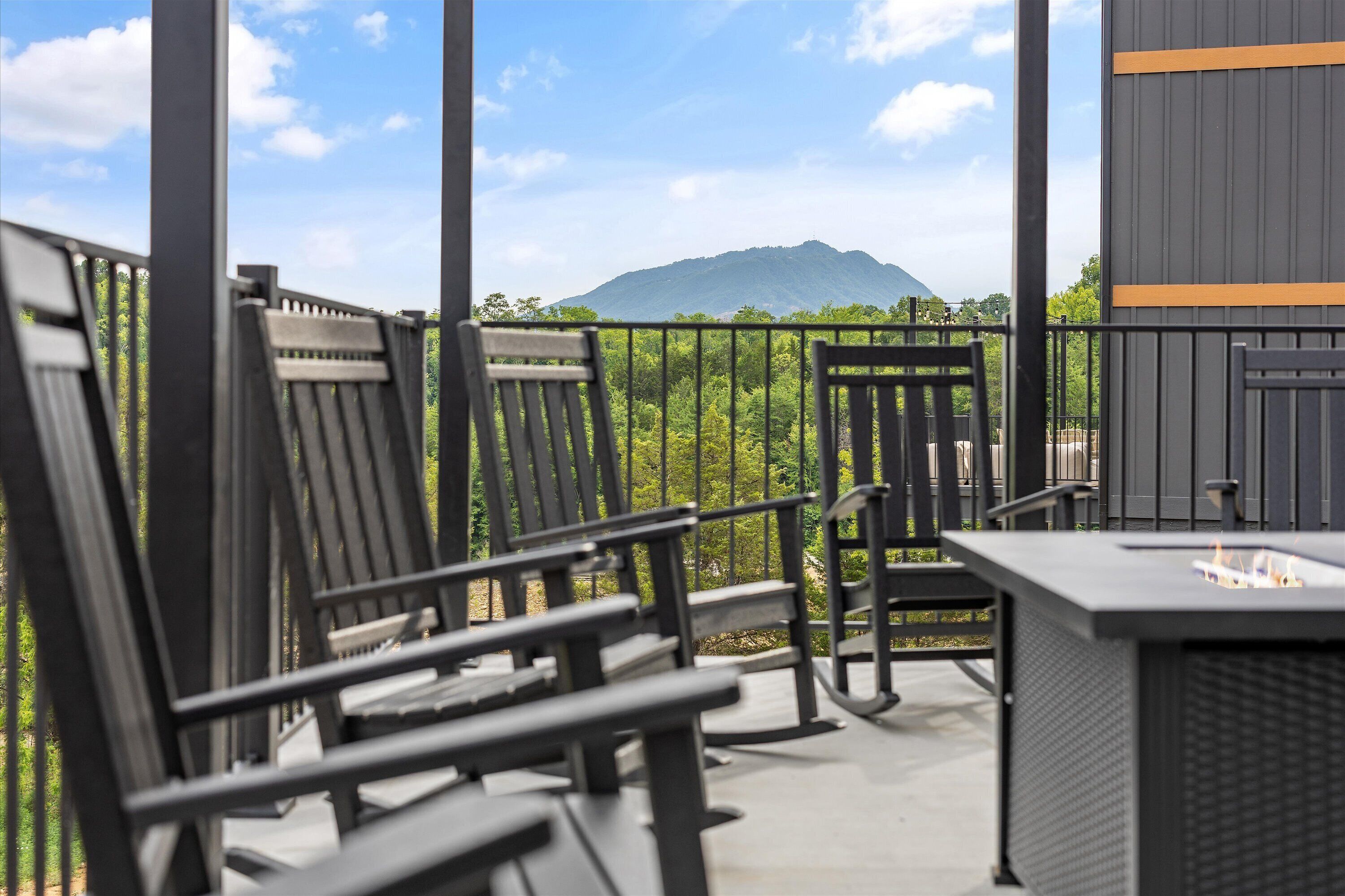 A balcony with chairs and a table, overlooking a mountain and greenery.