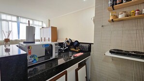 Una cocina moderna con encimera negra, microondas, fregadero y estufa. Hay armarios y una ventana con cortinas.