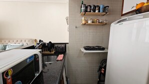 Una cocina compacta con microondas, pileta y estufa pequeña. Hay repisas sobre la estufa con distintos utensilios de cocina.