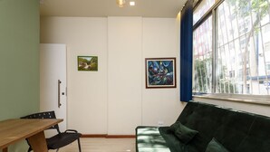 Ein Zimmer mit einem Holztisch, einem grünen Sofa und zwei gerahmten Kunstwerken an der Wand.