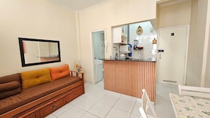A modern living room with a sofa, a wooden bar counter, a mirror, and a door leading to a bathroom. - Studio w/ AC | 5 min to Copacabana Beach (Rio de Janeiro)